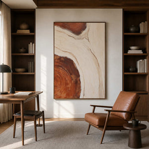 Wood framed cream and rust artwork beside bookshelves and a leather reading chair.