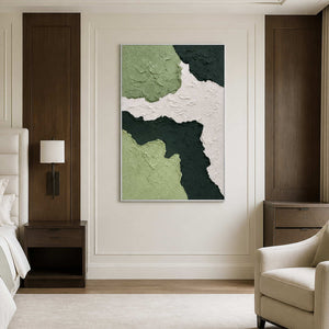 White framed green abstraction beside a neutral bed and upholstered reading chair.