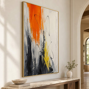 Vertical abstract artwork in orange, black, white, charcoal, and yellow, displayed in an entryway in a gold frame.