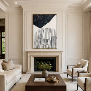 Gold framed black and ivory abstract painting above a fireplace in a living room.