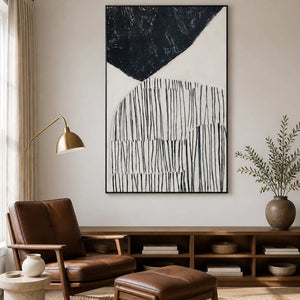 Black framed line painting above a low bookshelf beside a leather reading chair.