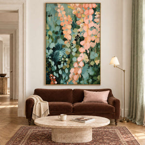 Cascading peach and blush leaves against deep green foliage in a gold frame, displayed above a sofa in a living room.