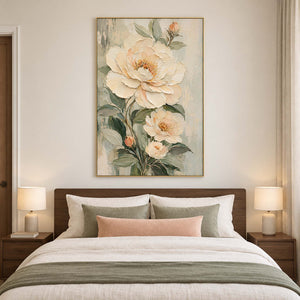 Cream flowers and soft green leaves on a muted background in a gold frame, displayed above a bed.