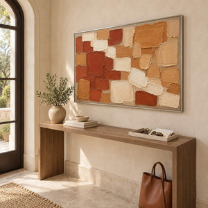 Terracotta, ochre, and cream raised block painting in a silver frame in an entryway.