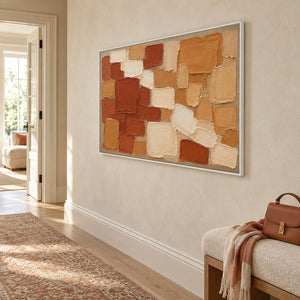 Terracotta, ochre, and cream raised block painting in a white frame in a hallway.