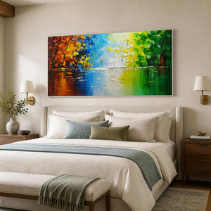 White-framed colorful lake painting above a cream bed with muted blue bedding.