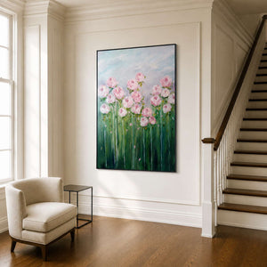 Black framed floral painting beside a cream armchair and wooden stairs in an ivory hall.
