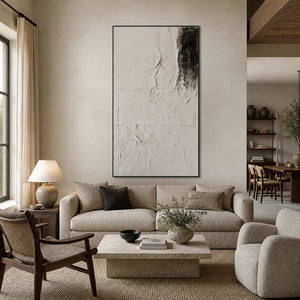 Black framed ivory abstract artwork above a cream sofa in a bright neutral living room.