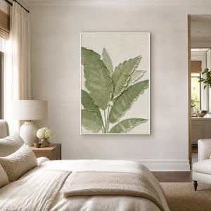 White-framed green leaf wall art displayed beside a bed in a calm neutral bedroom.
