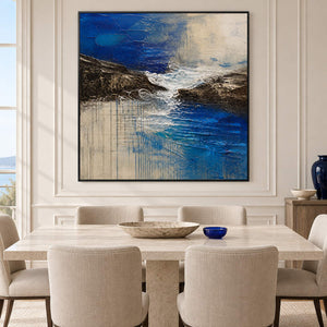 Square cobalt sea, dark rock, and ivory surf textured painting, displayed in a dining room in a black frame.