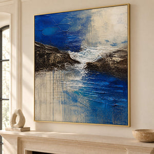 Square cobalt sea, dark rock, and ivory surf textured painting, displayed beside or above a fireplace in a gold frame.