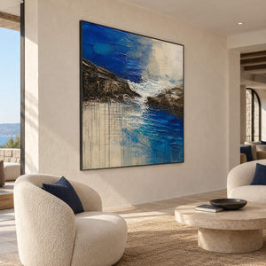 Square cobalt sea, dark rock, and ivory surf textured painting, displayed in a hotel lounge in a black frame.