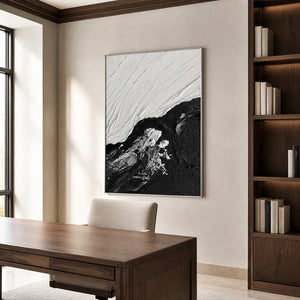 Silver framed black and white abstraction beside a wooden desk and dark bookcase.