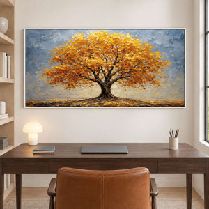 A broad golden autumn tree beneath a gray-blue sky in a white frame, displayed in a home office.