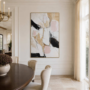 Gold framed abstract artwork beside a wooden dining table and cream upholstered chairs.