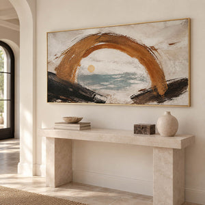 Hand-painted coastal abstract with a bronze arch sea-glass water and quiet sun, displayed in an entryway in a gold frame.