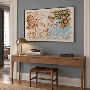 A Visit from Spring in a black frame above a wood hallway console and woven leather stool.