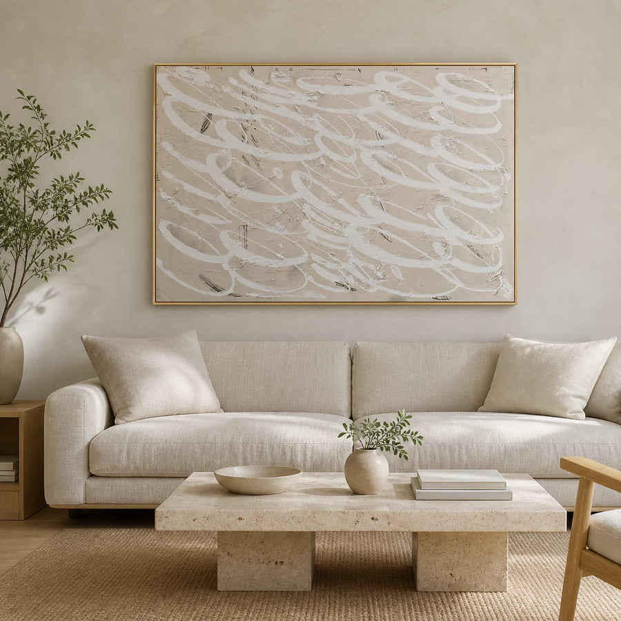 Gold framed white looping abstract art above a cream sofa and stone table.