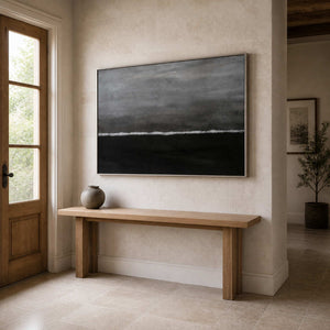Silver framed gray and black artwork above a wood console beside an entry door.