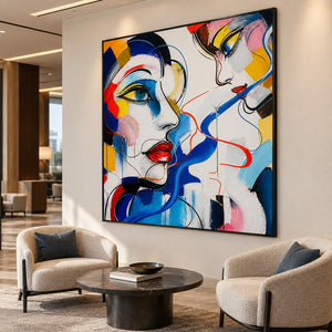 Hand-painted square portrait canvas with expressive faces and vivid color, displayed in a lounge in a black frame.