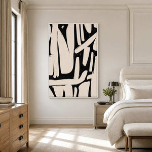 White framed cream and black abstract artwork beside a softly upholstered bed in neutral tones.
