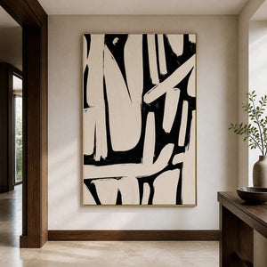 Gold framed cream and black abstract artwork beside a dark wooden console in a hallway.