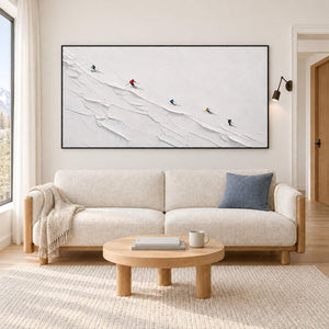 Tiny colorful skiers crossing a ridged white slope in a black frame, displayed above a sofa in a living room.