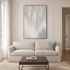 Soft gray and ivory vertical textures fading into pale blue in a black frame, displayed above a sofa in a living room.