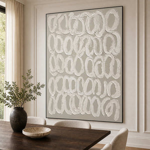 Black framed white loop artwork beside a dark wooden dining table and cream chairs.