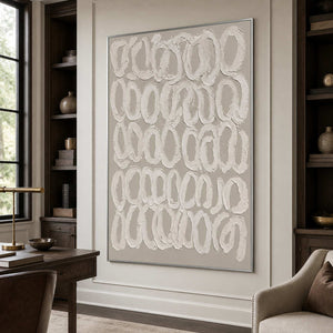 Silver framed white loop artwork between dark bookshelves beside a wooden home office desk.