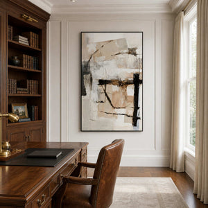 Black framed neutral abstract artwork beside bookshelves and a wooden desk in a bright study.
