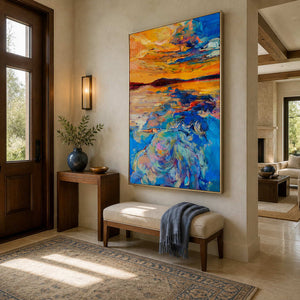 Silver framed vertical sunset artwork above an entry bench with a blue throw.