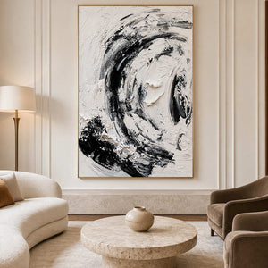 Gold framed black and white abstract painting beside a curved sofa and round stone table.