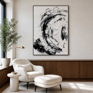 Black framed abstract painting beside a white reading chair, matching ottoman, and leafy tree.