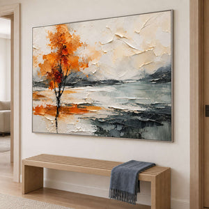 An orange autumn tree reflected beside a gray lake in a silver frame, displayed in a hallway.
