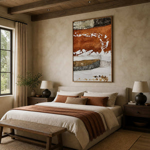 Wood framed vertical abstract artwork above a cream bed with rust colored pillows and throw.
