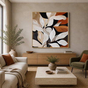 Gold framed botanical painting with cream and rust leaves in a bright living room.