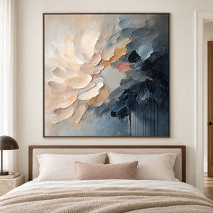 Layered cream and blush petals fading into deep blue in a brown wood frame, displayed above a bed.