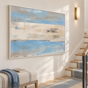 Pale blue and ivory coastal abstract painting with sand and charcoal bands in a white frame on a stair landing.