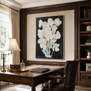 Silver framed cream floral artwork above a wooden desk between dark bookshelves.