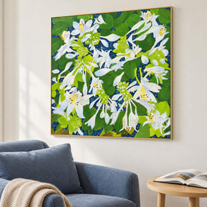 In a seating area, an artwork with a gold-colored frame shows white flowers and broad green leaves over a deep blue ground.