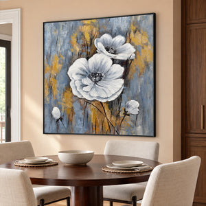 Two large white flowers and small buds on a blue-gray ground with ochre marks in an artwork with a black frame, displayed in a dining area beside the table.