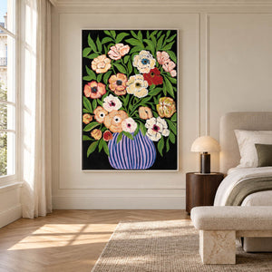 In a bedroom near the bed, an artwork with a white frame shows cream, peach and red flowers with green leaves in a purple-blue striped vase on black.