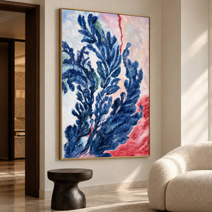 Branching deep blue forms curling upward over pale pink, cream and red in an artwork with a gold-colored frame, displayed in a seating area.