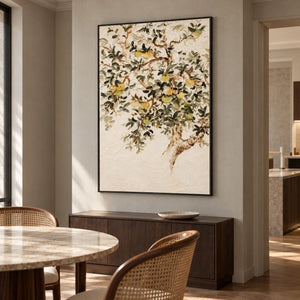 Artwork showing branching gray-green leaves and pale yellow-green fruit on cream in a dining area beside the table, with a black frame.
