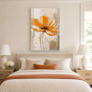 White framed orange floral artwork above a cream bed with orange cushion and throw.