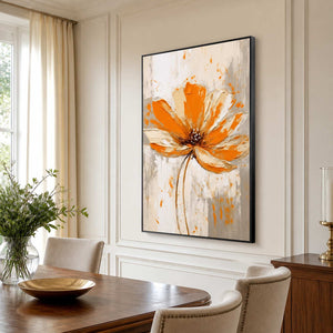 Black framed orange flower painting beside a wooden dining table with cream upholstered chairs.
