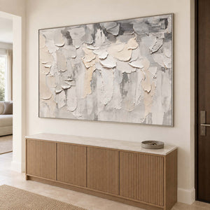 Overlapping ivory and gray raised strokes on a pale ground in a silver frame, displayed above an entryway console.