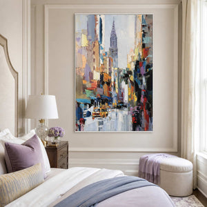 White framed colorful cityscape beside a bed with lavender pillows and pale blue bedding.