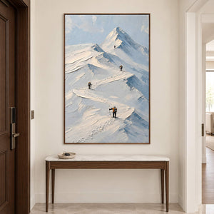 Small climbers following ridges across snowy mountains in a brown wood frame, displayed above an entryway console.